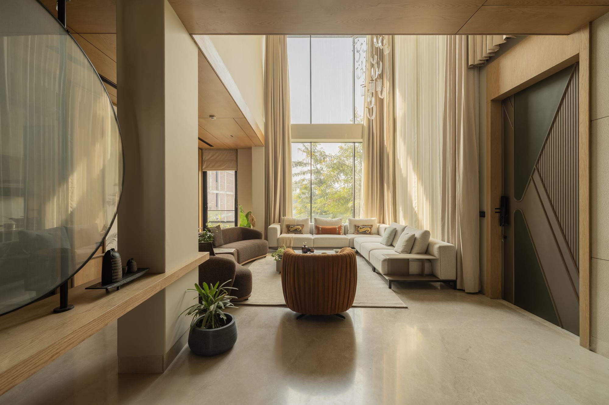 A double-height living room with sheer curtains and deep daylight